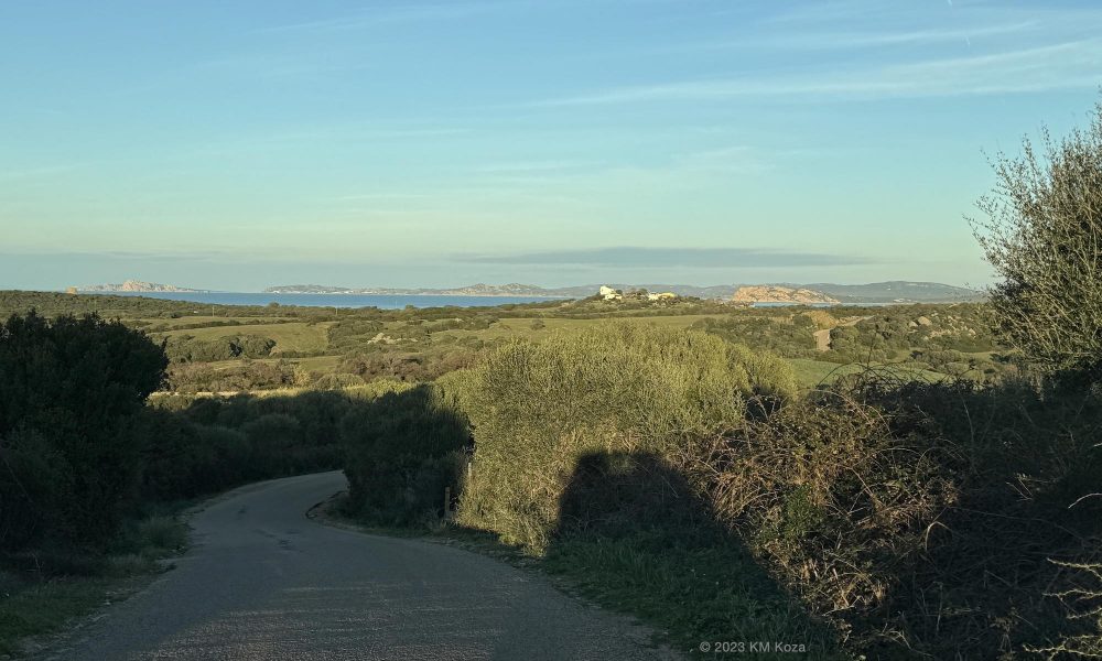 View of road through gentle hills to sea with distant coast in Gallura, Sardinia.